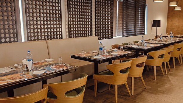 A dining area with multiple tables set for meals, each with plates, cutlery, and water bottles. - The Mayberry A Bergamont Hotel Tiruppur (Tirupur)