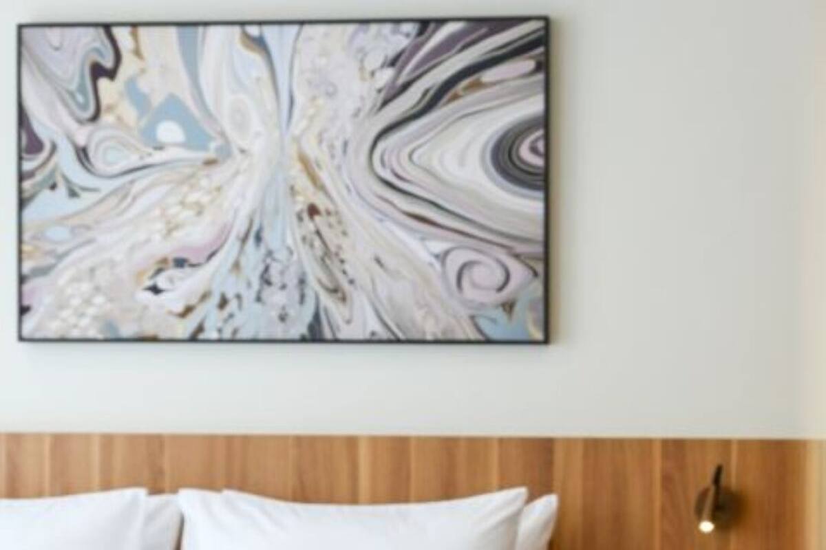 Una cama con ropa de cama blanca, un cabecero de madera y un cuadro abstracto colgado en la pared.