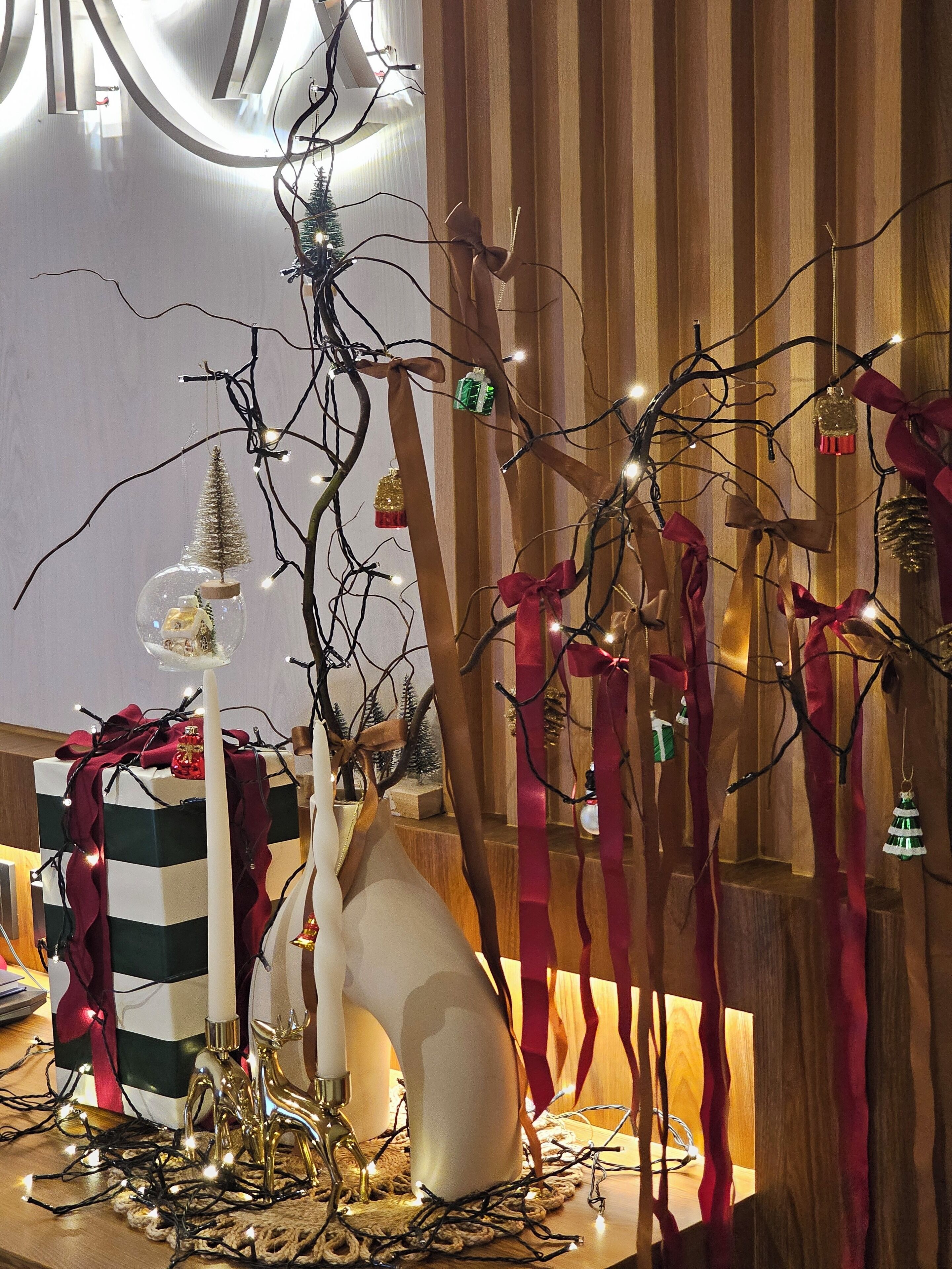 Une pièce avec un mur recouvert de lambris en bois, un vase blanc, un coffret cadeau à rayures et un petit sapin de Noël.