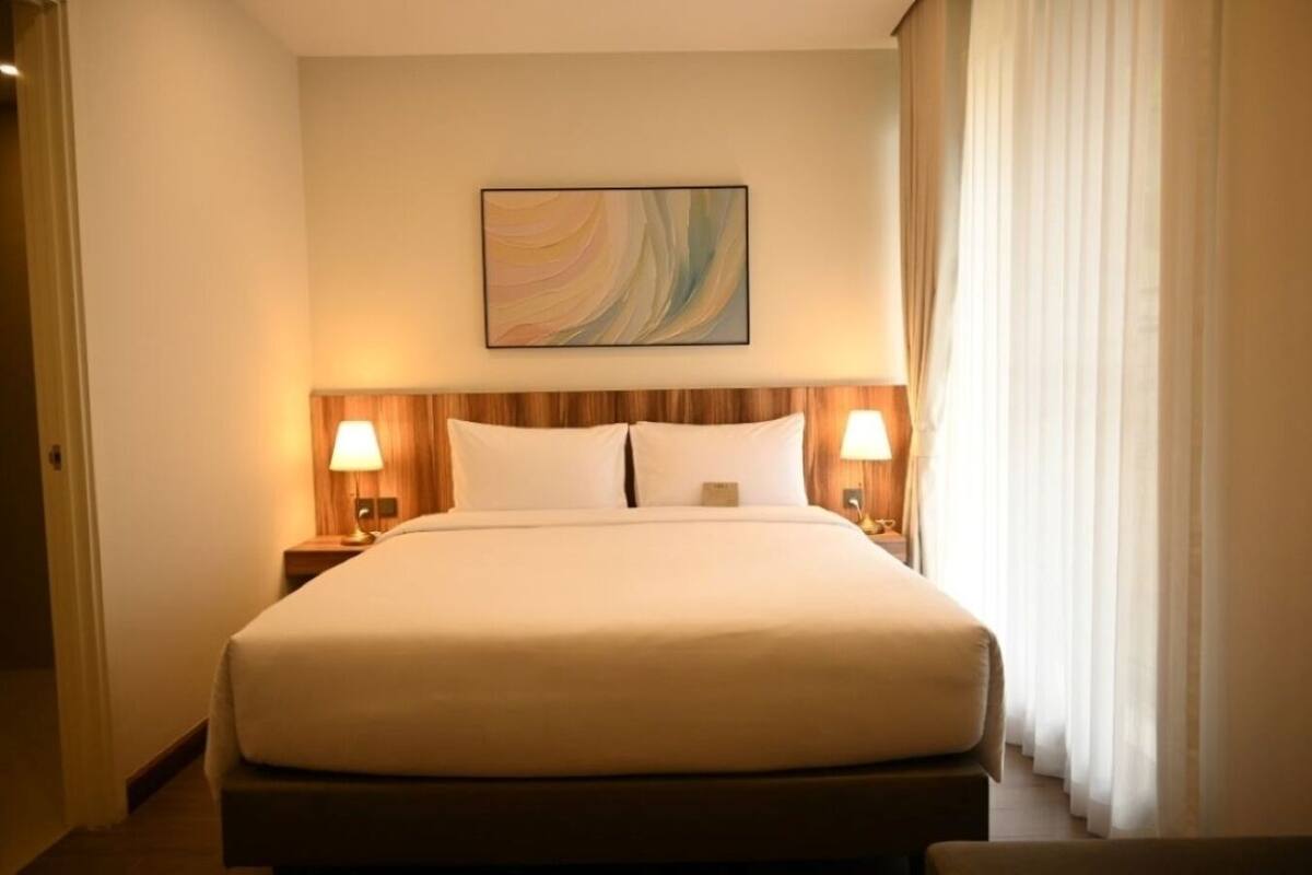 Una habitación de hotel con una cama grande, dos lámparas de noche, un cuadro en la pared y una ventana con cortinas.