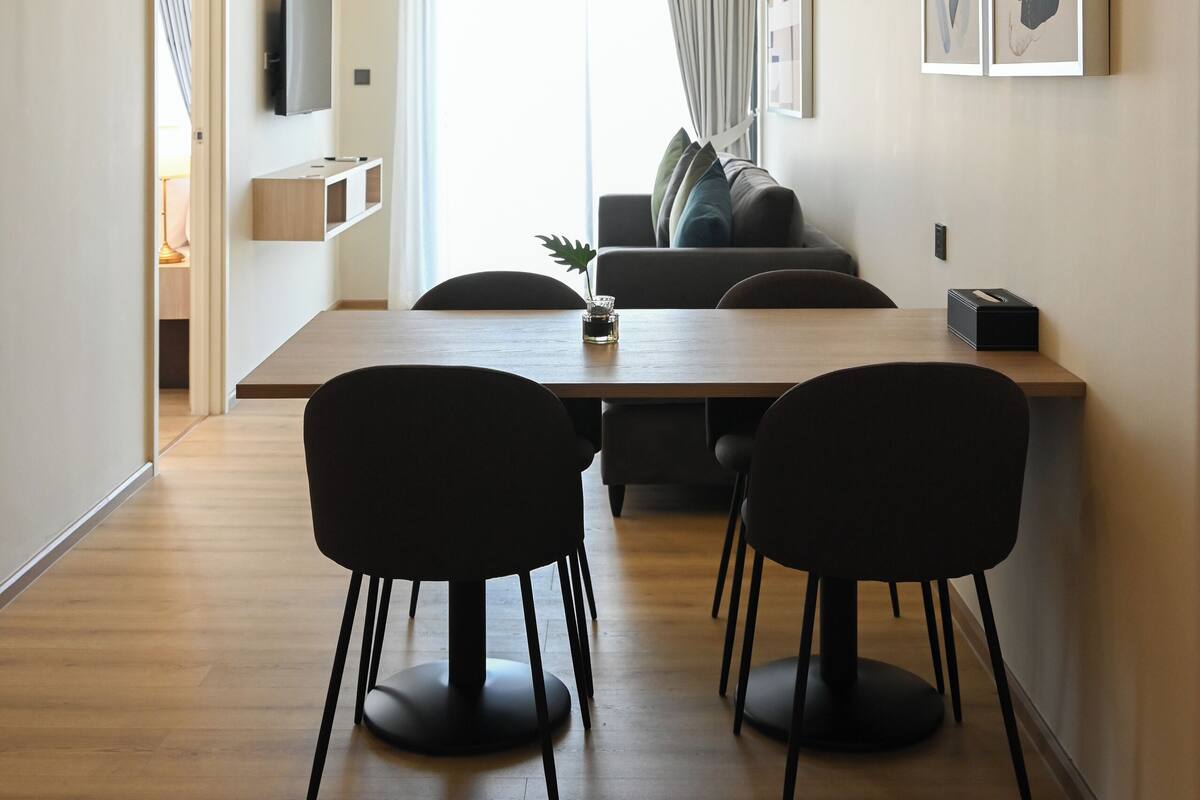 Una sala de estar moderna con un sofá, una mesa de comedor con sillas, un televisor de pantalla plana en la pared y un amplio ventanal con cortinas.