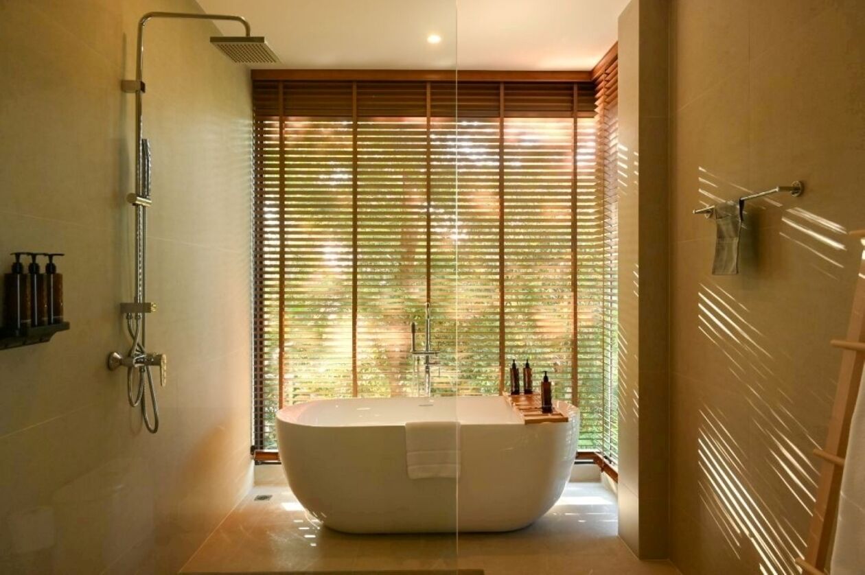 A modern bathroom with a freestanding bathtub, a showerhead, and a window with blinds.