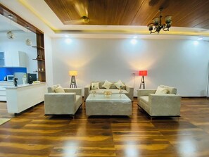 Uma sala de estar espaçosa com teto de madeira, dois sofás, uma mesa de centro e duas luminárias de chão.