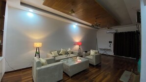 A spacious living room with a high ceiling, wooden beams, and a modern chandelier. There are two sofas and a coffee table with decorative items. - Luxury 3BHK Villa Stay Royal in Aerocity Mohali (Mohali)