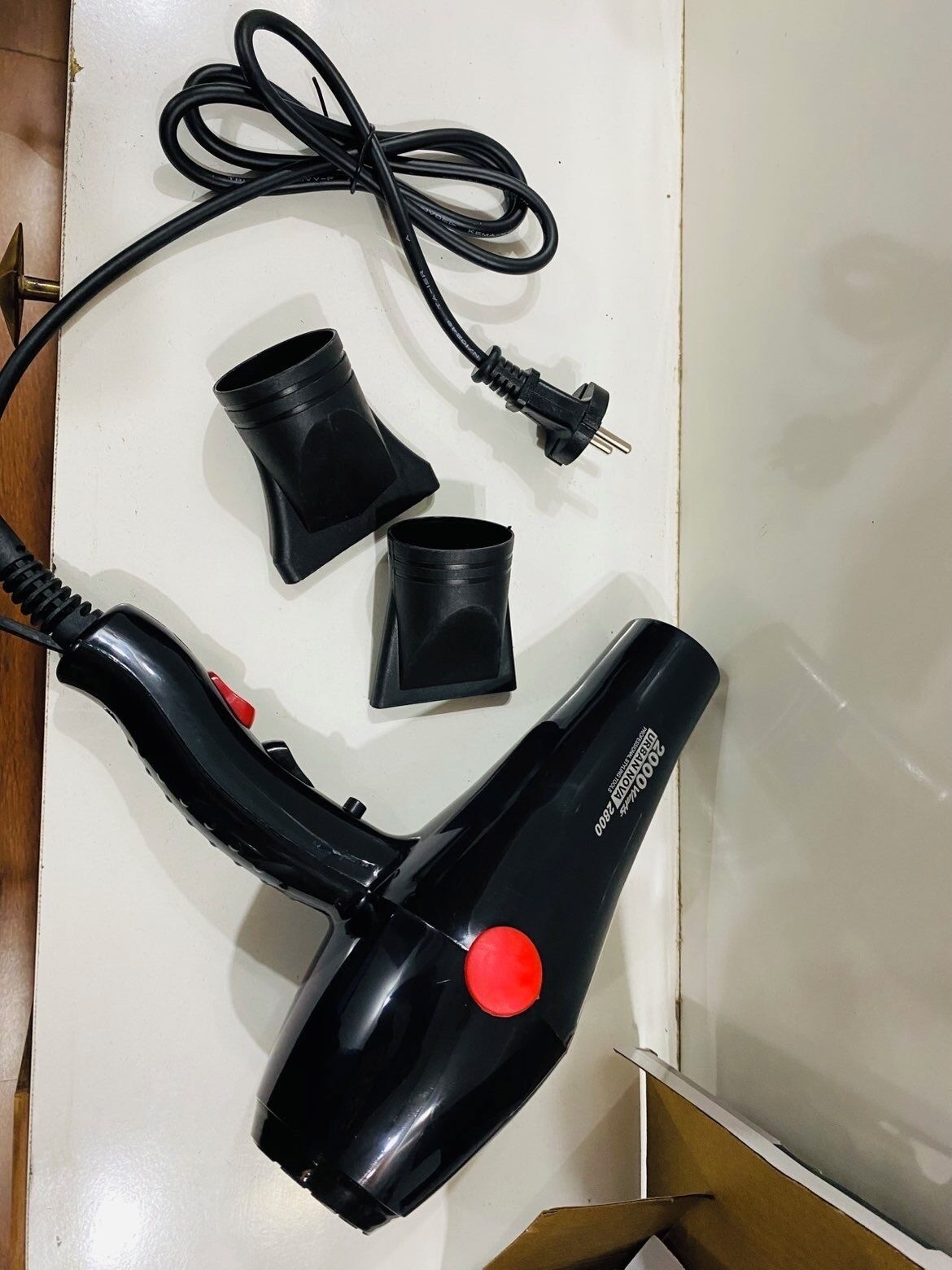 Un sèche-cheveux doté d’un bouton rouge, d’un cordon d’alimentation noir et de deux récipients en plastique noir.