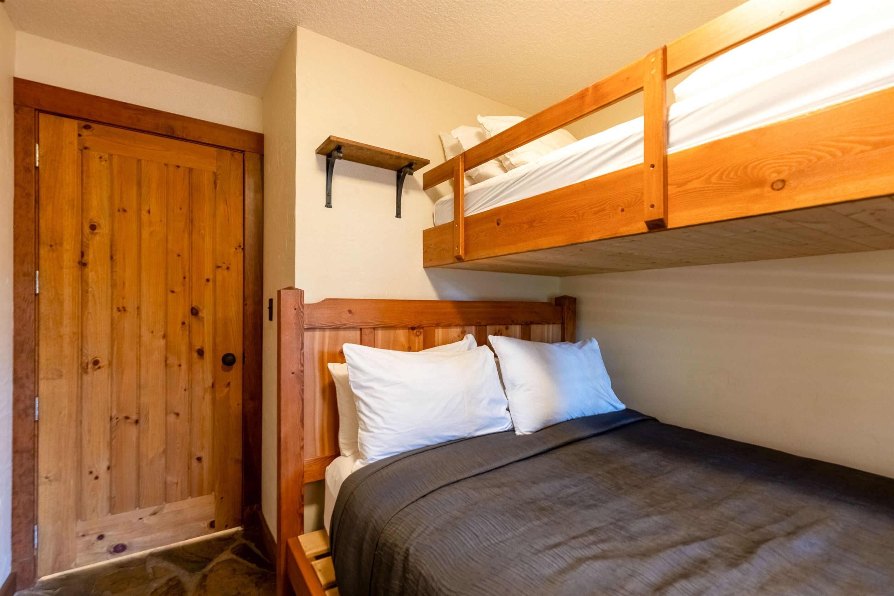Een stapelbed met een houten hoofdbord, een houten deur en een klein plankje boven het bed.