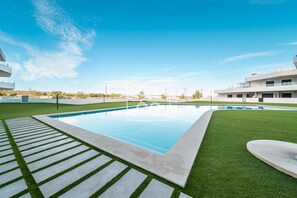 Ein moderner Poolbereich mit blauem Himmel, umgeben von gepflegtem Rasen und einem befestigten Gehweg.