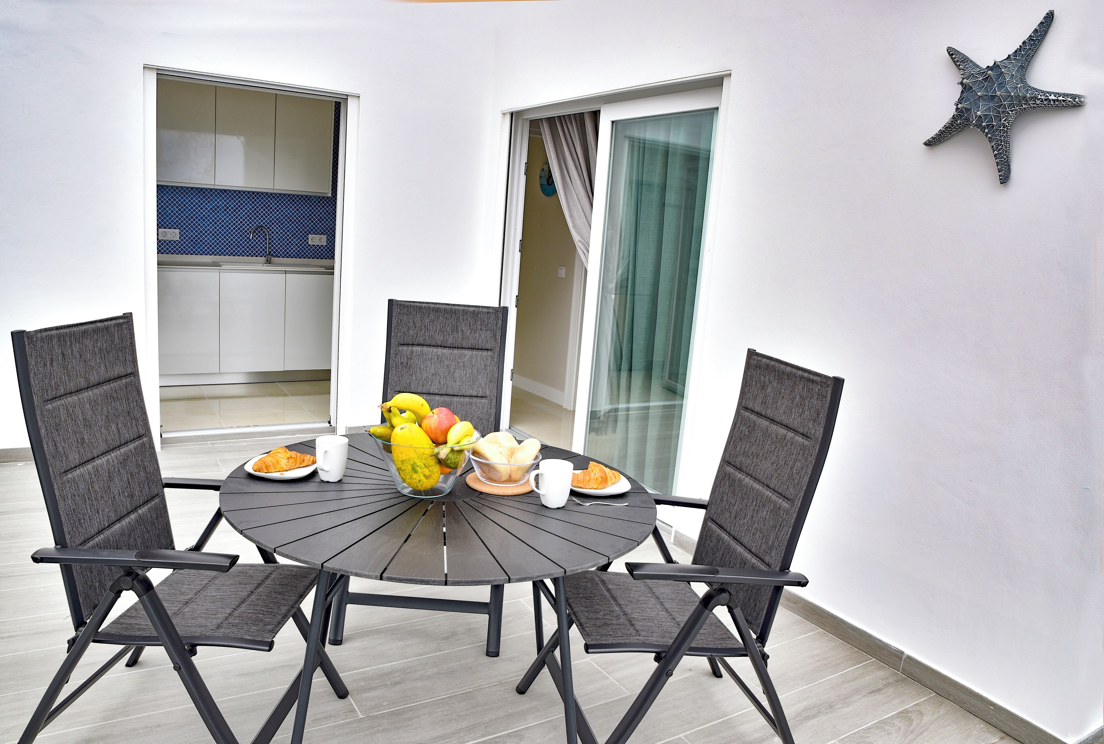 A round table with four chairs, a starfish decoration, and a breakfast setting with fruits and pastries.