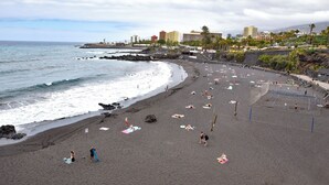 A beach with a volleyball court, umbrellas, and people sunbathing.