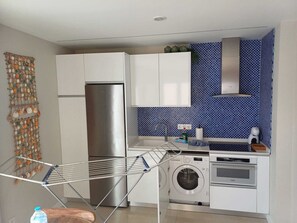 A modern kitchen with white cabinets, a stainless steel refrigerator, a washing machine, and a drying rack. - ATLANTIC GETAWAY LA SIRENA PLAYA B (Puerto de la Cruz)