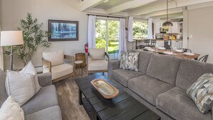 A living room with a sofa, armchair, coffee table, and a dining area with a table set for four. - Ski. Hike. Soak. Dogs Welcome | Nordic Ski Haus (Big Sky)