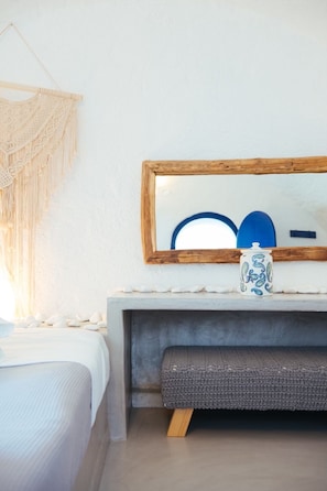 A bedroom with a bed, a bedside table, a mirror, and a wall-mounted macrame piece.