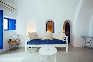 A white sofa with blue cushions, a small round table, and a white chair in a room with white walls and blue accents.