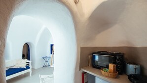 A compact kitchenette with a microwave, toaster, and bread basket. A white bench and a small table are visible in the background.