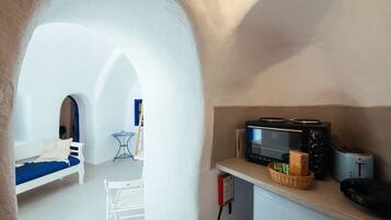 Eine kompakte Küchenzeile mit Mikrowelle, Toaster und Brokkorb. Im Hintergrund sind eine weiße Bank und ein kleiner Tisch zu sehen.