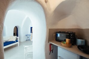A compact kitchenette with a microwave, toaster, and bread basket. A white bench and a small table are visible in the background.