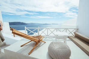 A balcony with a wooden lounge chair, a white cushioned bench, and a white railing.