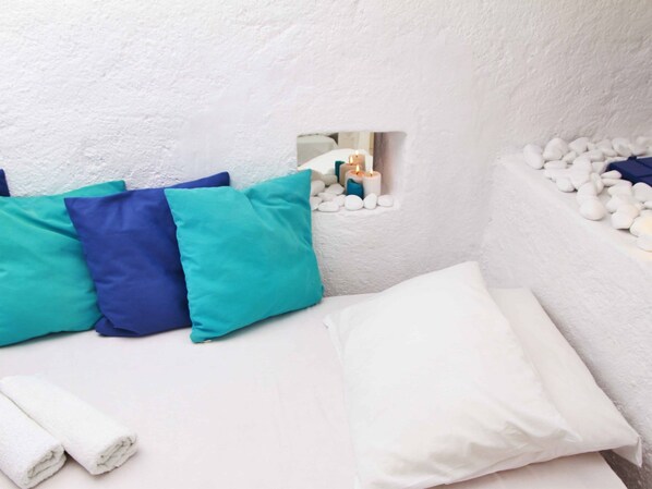 A room with a white textured wall, a small window with a mirror, and a bed with white and teal pillows.
