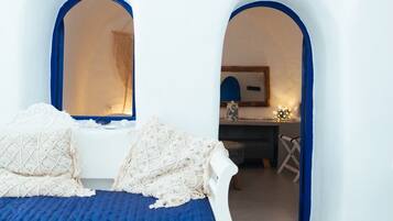 Ein weißes Bett mit blauer Bettwäsche in einem Raum mit weißen Wänden und blauen Rundbögen.