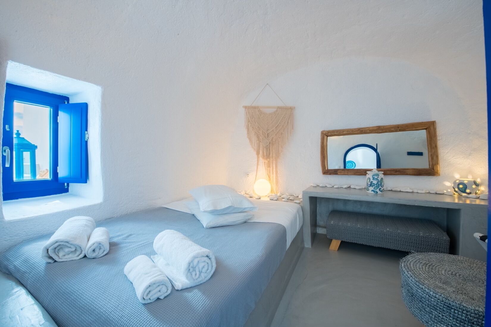 Ein Schlafzimmer mit Bett, Nachttisch, Spiegel und einem Fenster mit blauen Fensterläden.
