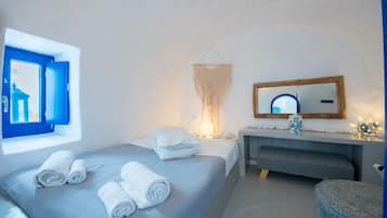 Ein Schlafzimmer mit Bett, Nachttisch, Spiegel und einem Fenster mit blauen Fensterläden.