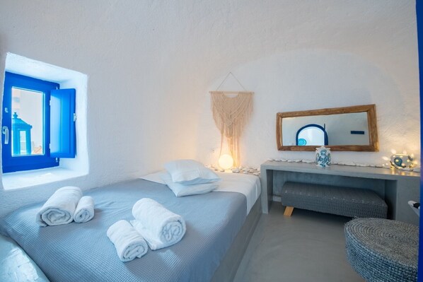 A bedroom with a bed, a bedside table, a mirror, and a window with blue shutters.