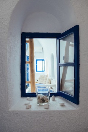 A room with a large window, a bed, and a small table with stones. - Blu Bianco cave loft (Oia)