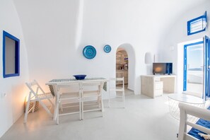 A modern, white-walled room with a dining area, a TV, and a view of the sea.