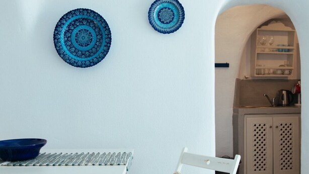 A white dining table with two chairs, a blue bowl, and two decorative plates on the wall.