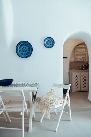 A white dining table with two chairs, a blue bowl, and two decorative plates on the wall.