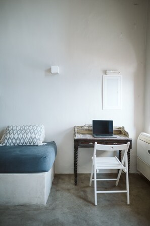 Een kamer met een bed, een bureau met een laptop, een radiator en een lichtschakelaar op de muur.