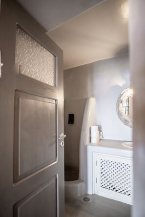 A bathroom with a wooden door, a white sink with a mirror, and a shower area.