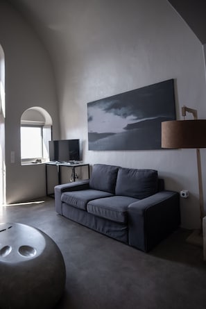 A modern living room with a gray sofa, a flat-screen TV, a painting, and a lamp.
