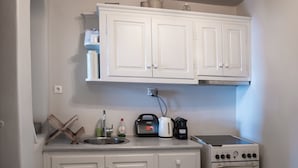 A compact kitchen with white cabinets, a stove, and a sink.