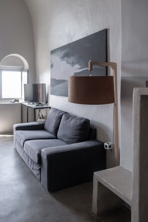 Een moderne woonkamer met een grijze bank, een tafeltje, een lamp en een schilderij aan de muur.