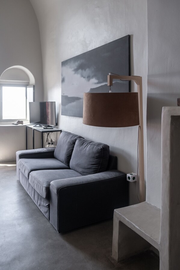 A modern living room with a grey sofa, a small table, a lamp, and a painting on the wall.