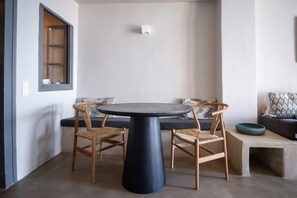 A room with a round table, two wicker chairs, a sofa with patterned cushions, and a small concrete bench.