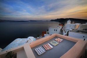 A rooftop terrace with a view of the sea, featuring a few cushions and a glass of wine.
