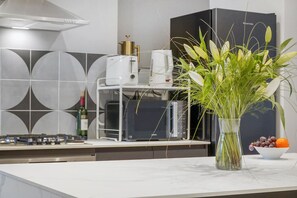 A modern kitchen with a white countertop, a stainless steel range hood, a white coffee machine, and a vase with green plants and fruit. - Bright stylish N. London retreat (Greater London)