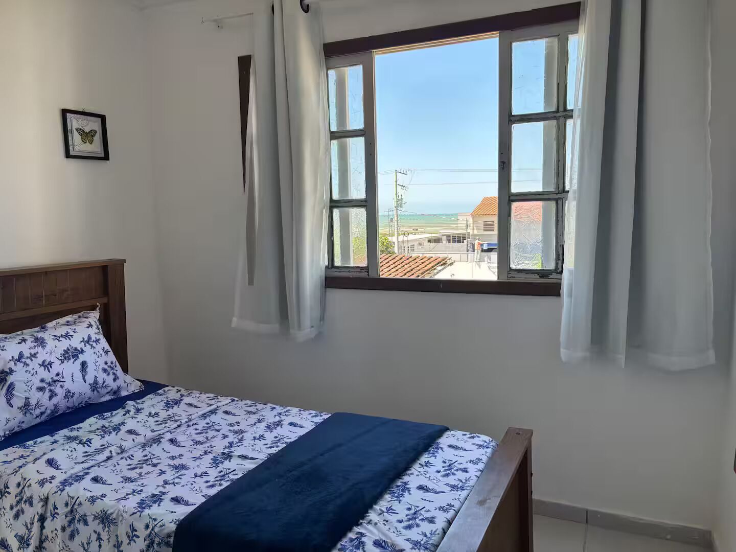 Ein Schlafzimmer mit einem Bett, einem Fenster mit Vorhängen und Blick auf Gebäude.