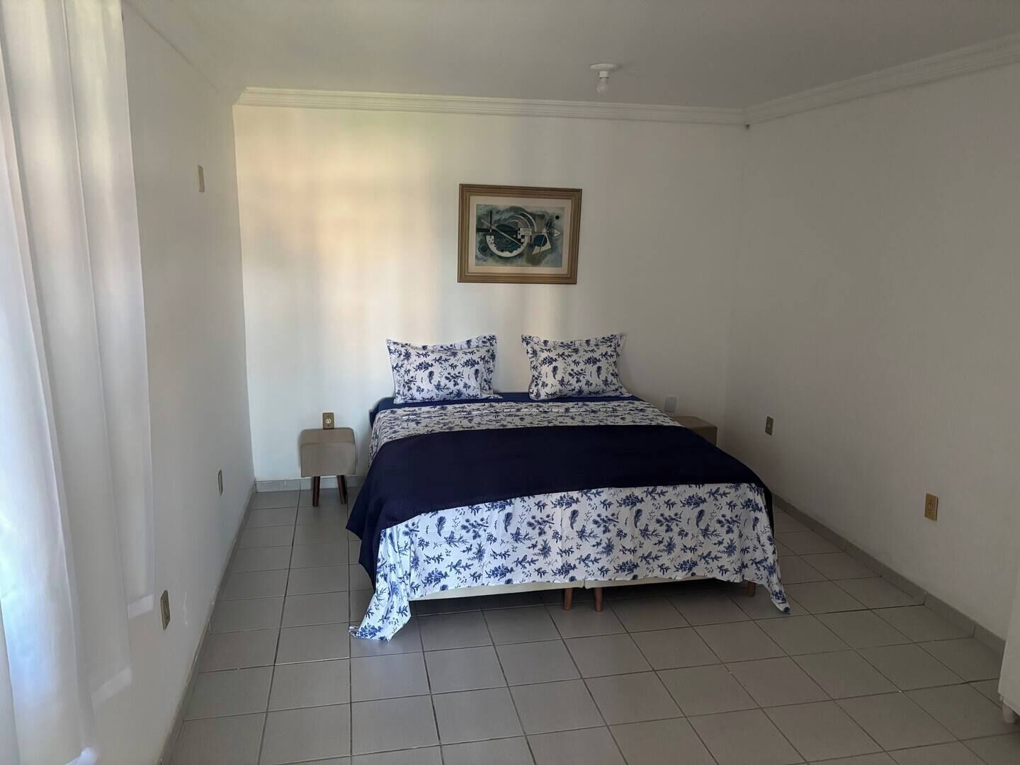 A bedroom with a bed, a nightstand, a small table, and a framed picture on the wall.