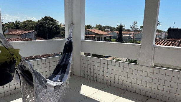 A balcony with a hammock, tiled floor, and a view of houses in the background. - Blue Wave Hostel (Serra)