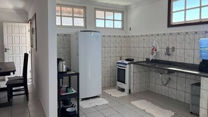 A kitchen with white tiled walls, a white refrigerator, a stove, a sink, and a water dispenser. - Blue Wave Hostel (Serra)