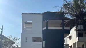 A multi-story building with a white and dark facade, a gated entrance, and a paved area in front. - Blue Wave Hostel (Serra)