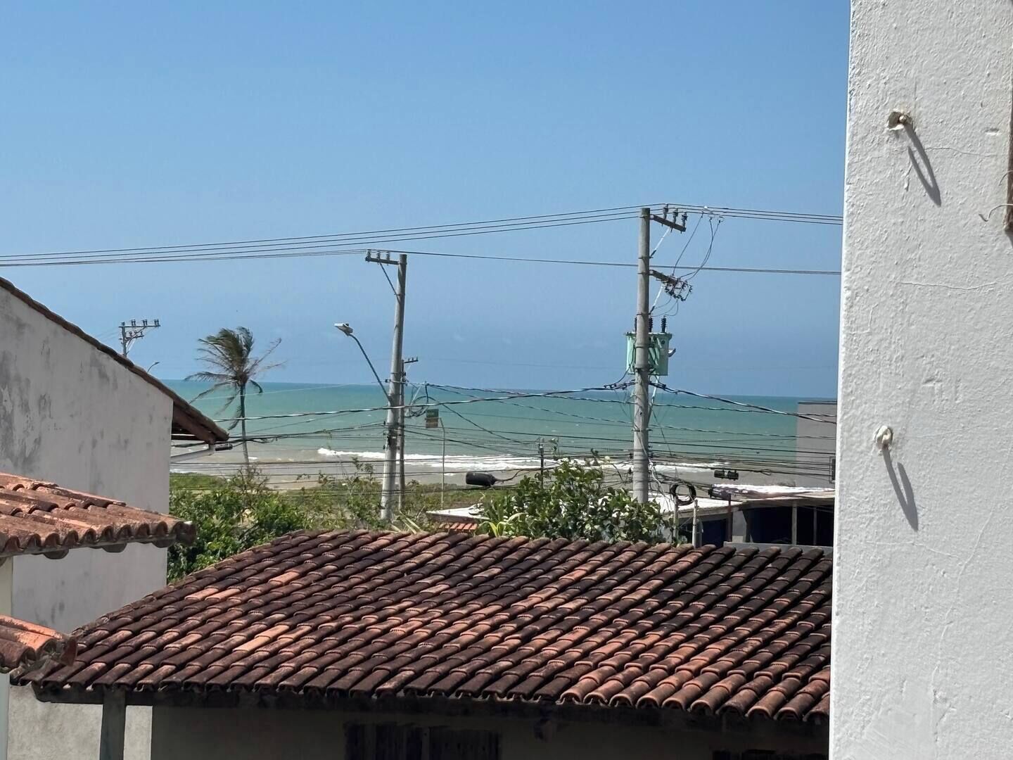 Vista costera con tejado de baldosas, líneas eléctricas y una playa al fondo.