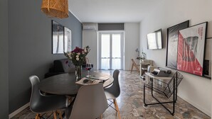 Un comedor moderno con una mesa redonda, sillas, un jarrón con flores y una copa de vino tinto.
