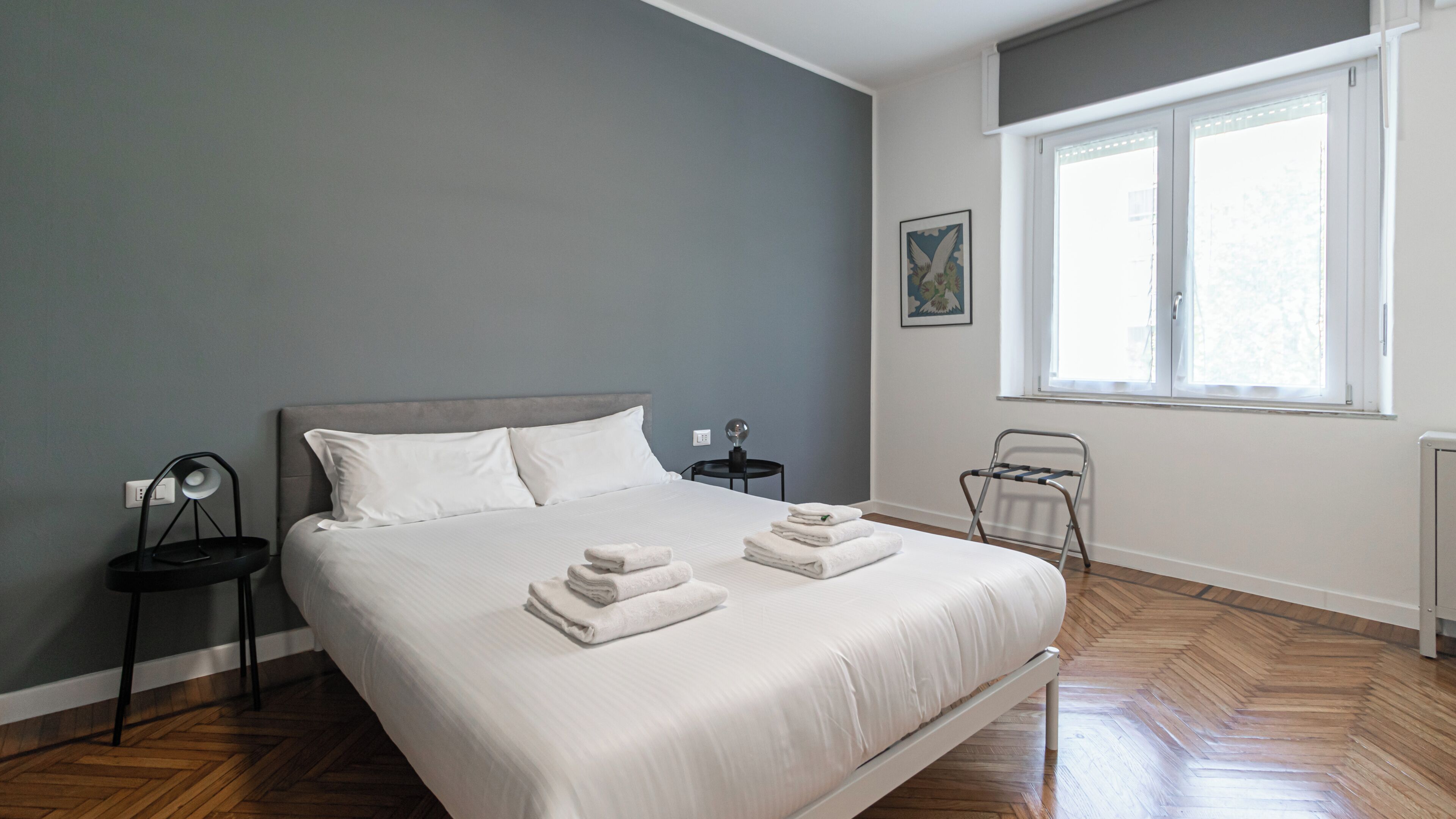 Une chambre moderne avec un grand lit, une lampe de chevet, un radiateur et une fenêtre avec des stores.