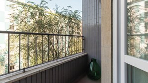 Un balcón con barandilla metálica, una planta en maceta y vistas a árboles y edificios.