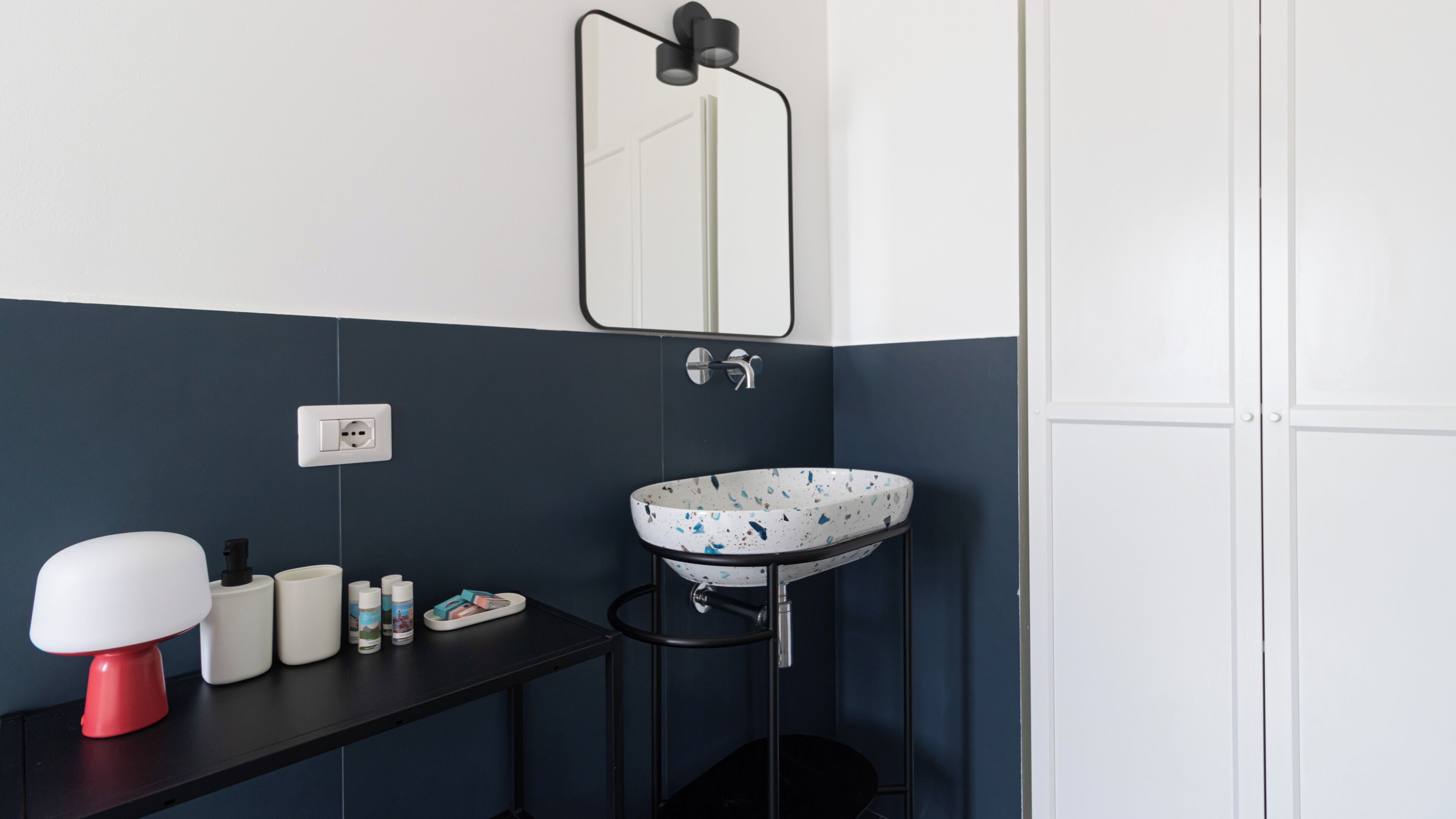 Un baño con lavamanos blanco, espejo y encimera negra.
