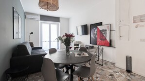 Una sala de estar moderna con comedor, que incluye un sofá, sillas, una mesa con un florero y un televisor montado en la pared.